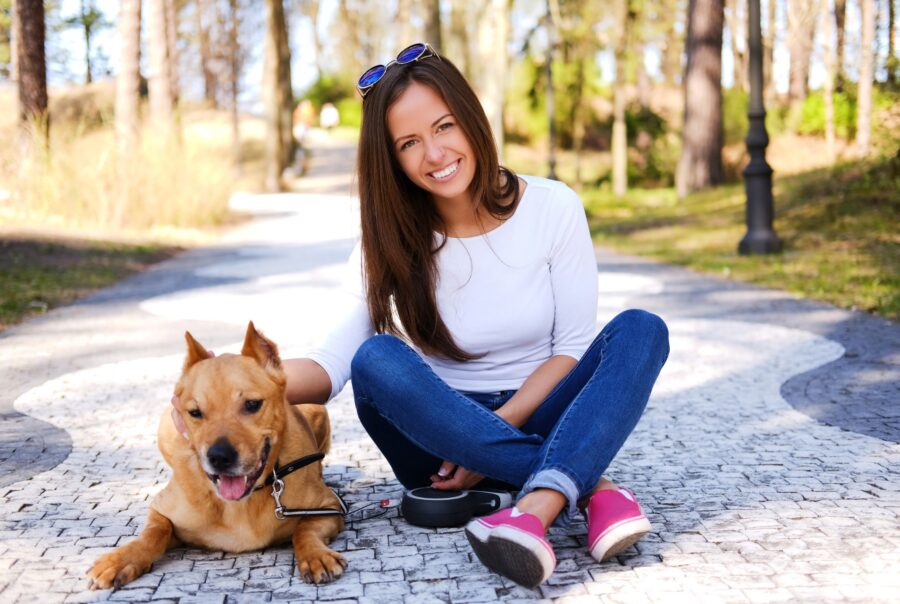 Una mujer sentada con un perro marrón en un camino pavimentado.