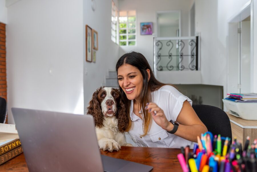 Una mujer con un cocker en su regazo mientras usa una laptop en una mesa.