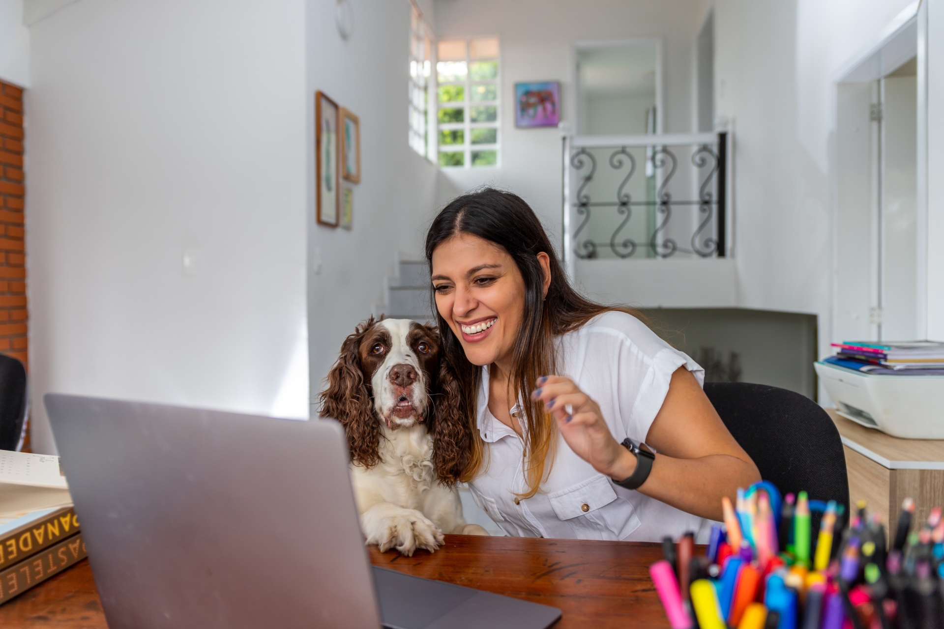 Una mujer con un cocker en su regazo mientras usa una laptop en una mesa.