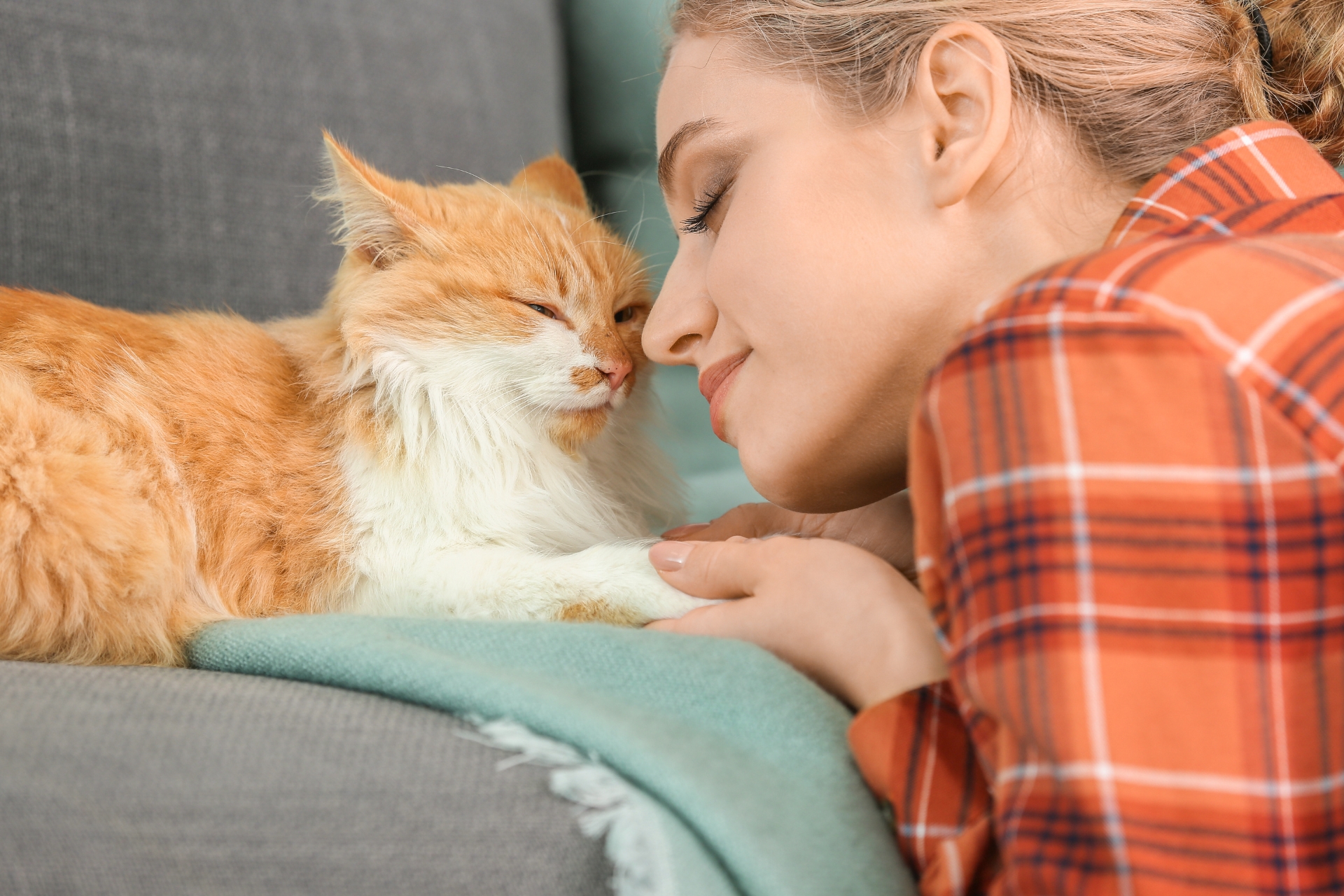Una mujer besando a un gato naranja en un sofá.