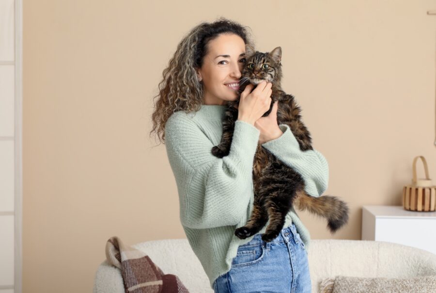 Una mujer abrazando a un gato rayado en una sala con sofá.